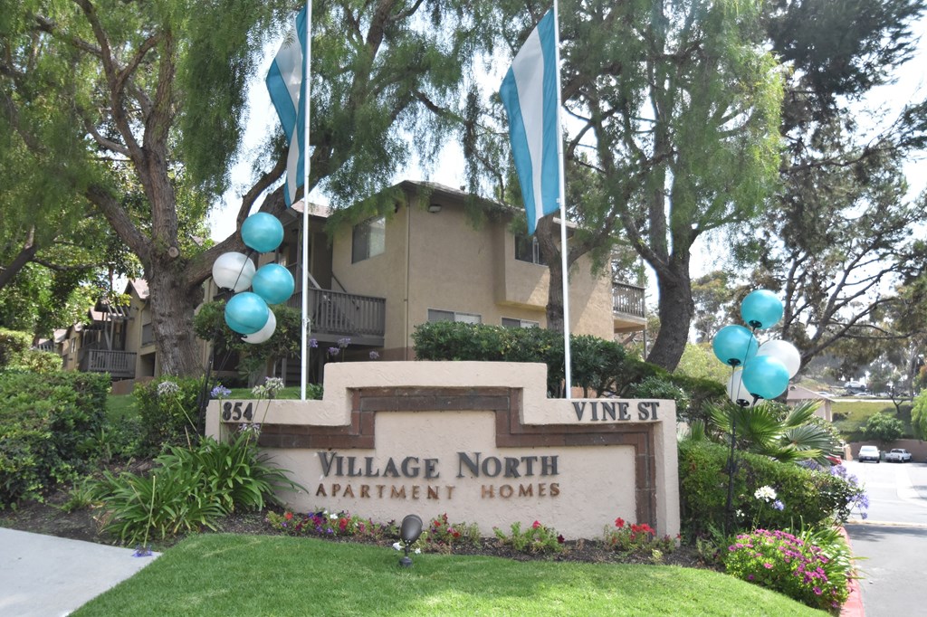a photo of the village north apartment homes sign with blue and white balloons above it