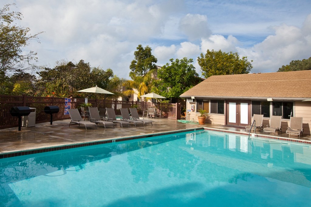 a pool with lounge chairs and umbrellas next to a house