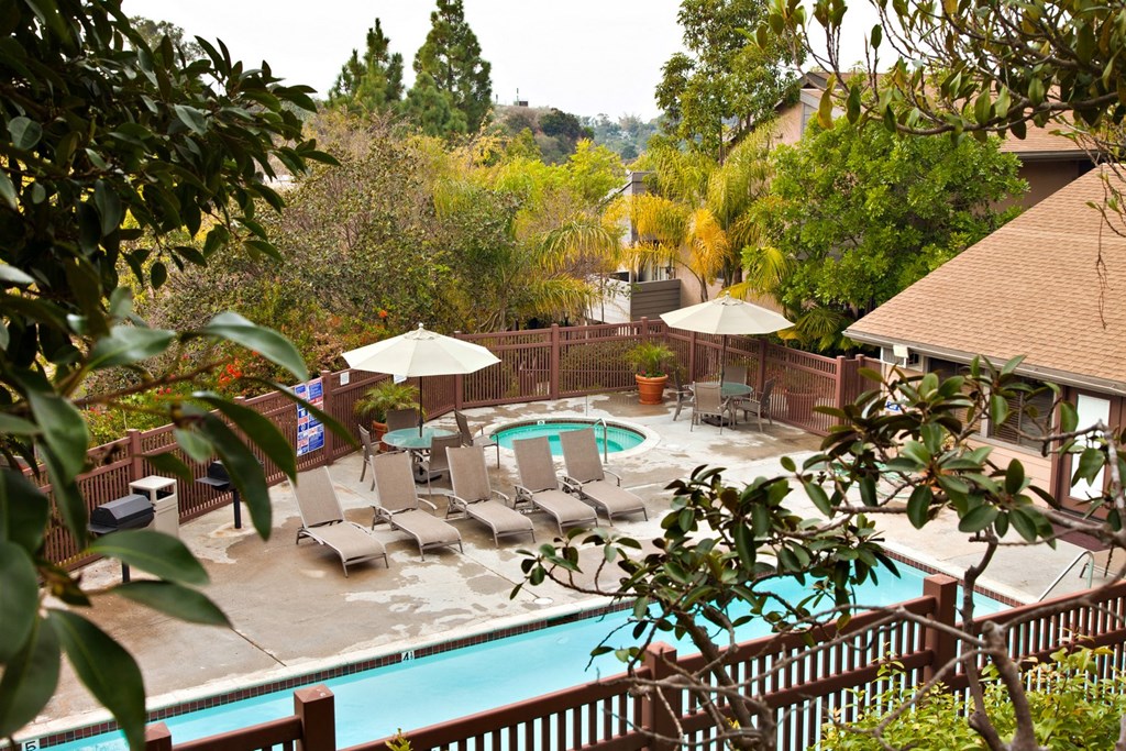 a pool with lounge chairs and umbrellas in front of a house
