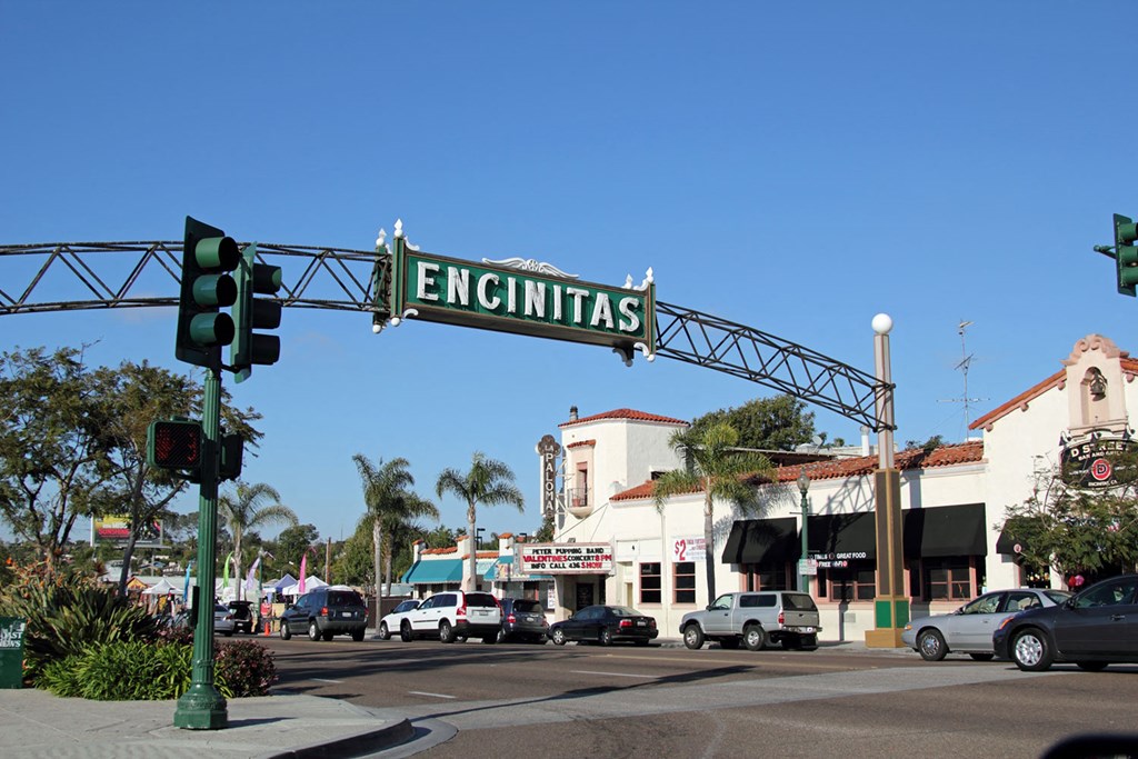 a green and white sign hangs over a street with cars parked on the side of the road