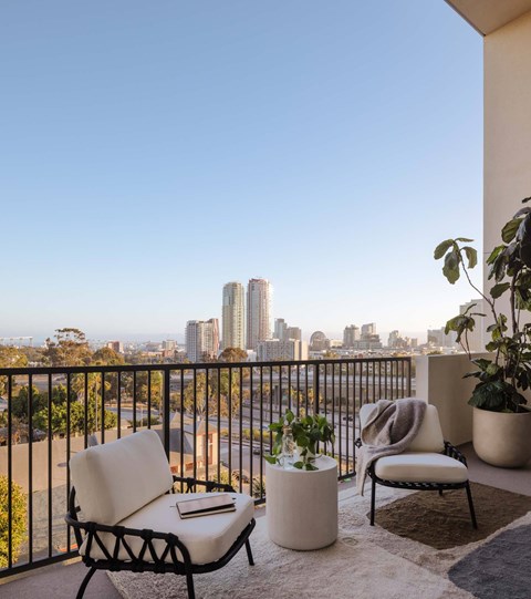 A balcony with a chair, table, and potted plant overlooking a city skyline.