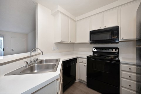 A black oven sits under a microwave in a white kitchen.