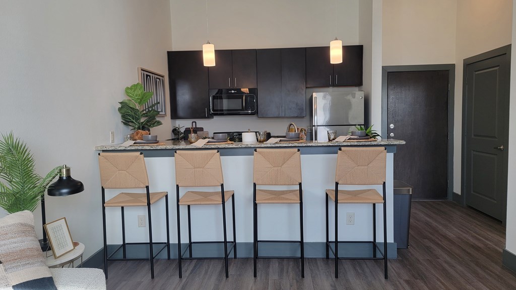 A kitchen with black cabinets and a bar area with four chairs at Urban Square, Denton, TexasX, 76210