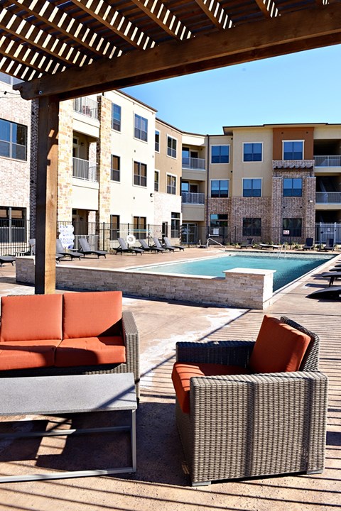 an outdoor lounge area with chairs and a pool at an apartment complex