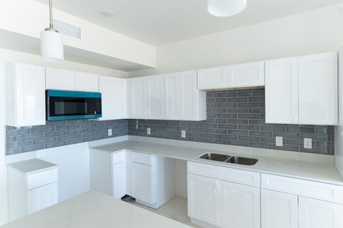 A kitchen with white cabinets and a blue backsplash.