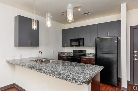 SevenTwelve Lofts Downtown UNT Denton Apartments A kitchen with granite countertops and black appliances.