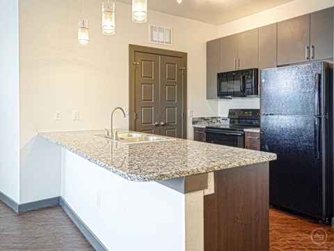 SevenTwelve Lofts Downtown UNT Denton Apartments A kitchen with a granite countertop and a black refrigerator.