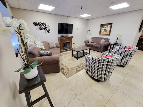 A living room with a brown couch, a television, and a vase of white flowers.