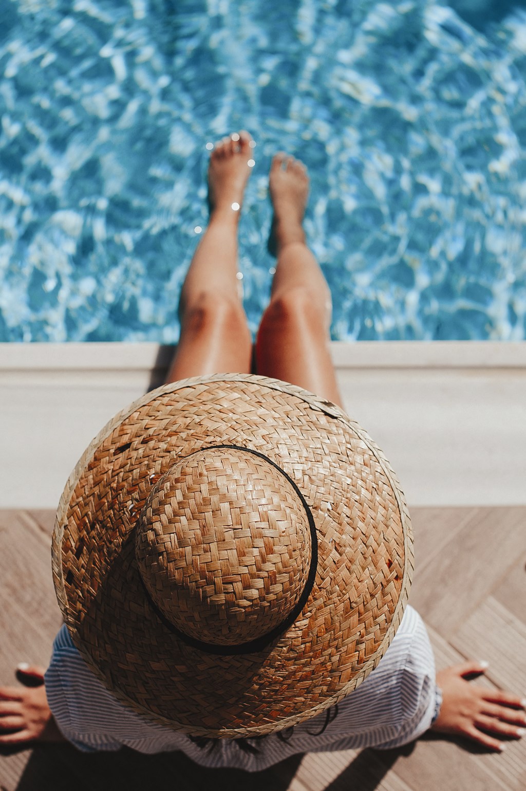 a woman with a straw hat laying on the floor next to a pool