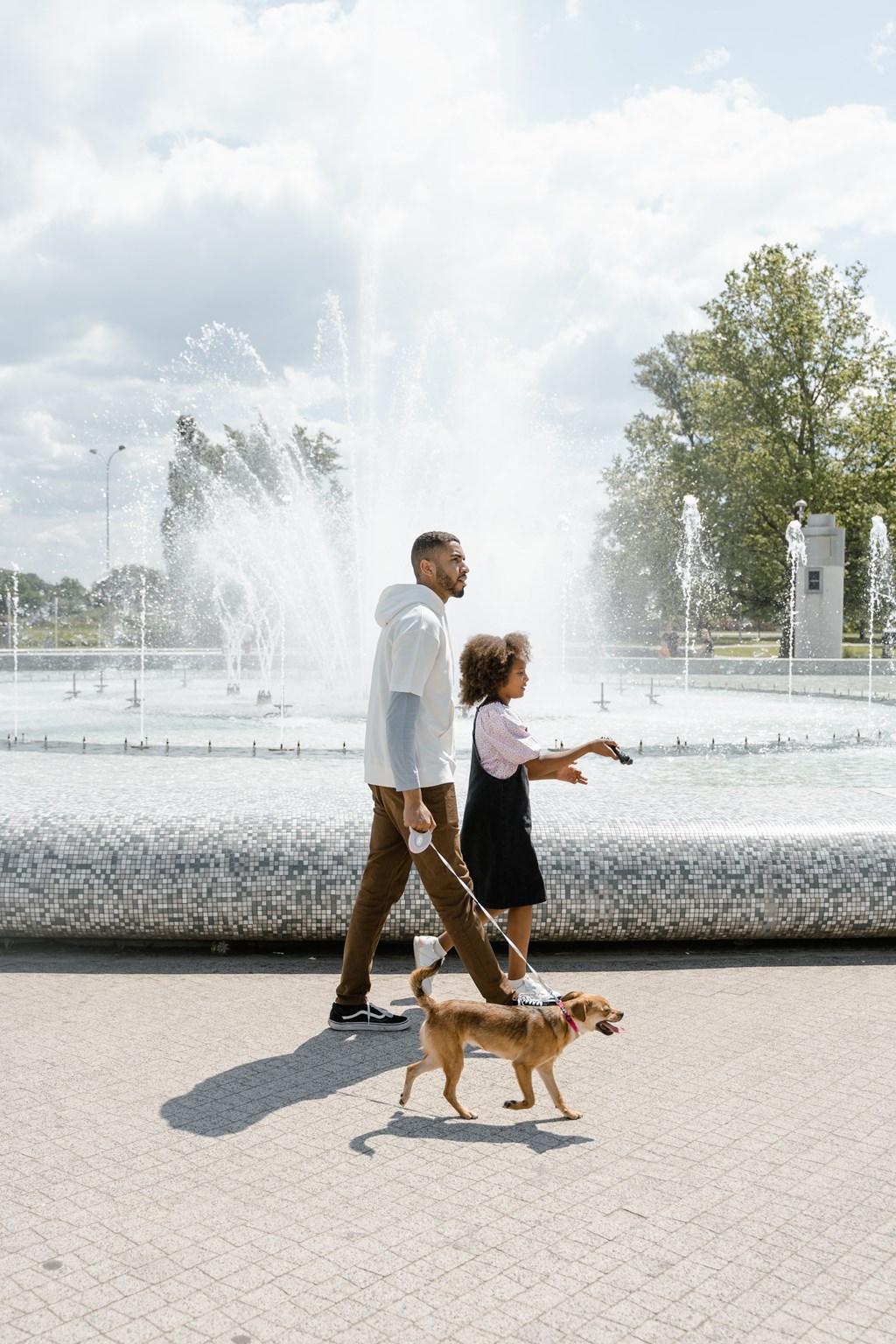 a man and woman walking their dog in front of a fountain