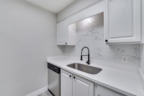 A kitchen with white cabinets and a marble backsplash.