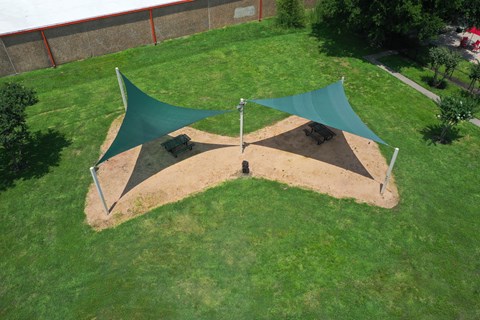 A green and brown shade structure in a grassy area.