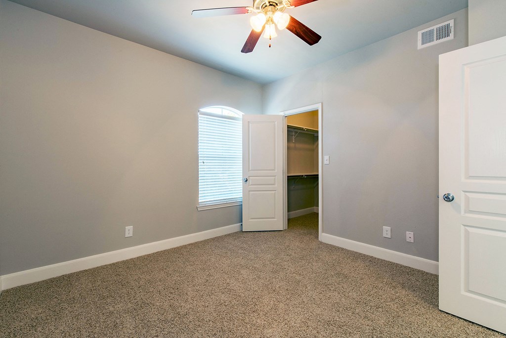 an empty bedroom with a ceiling fan and a door to a bathroom