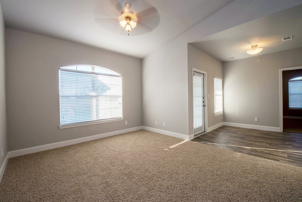 an empty living room with a large window and a ceiling fan