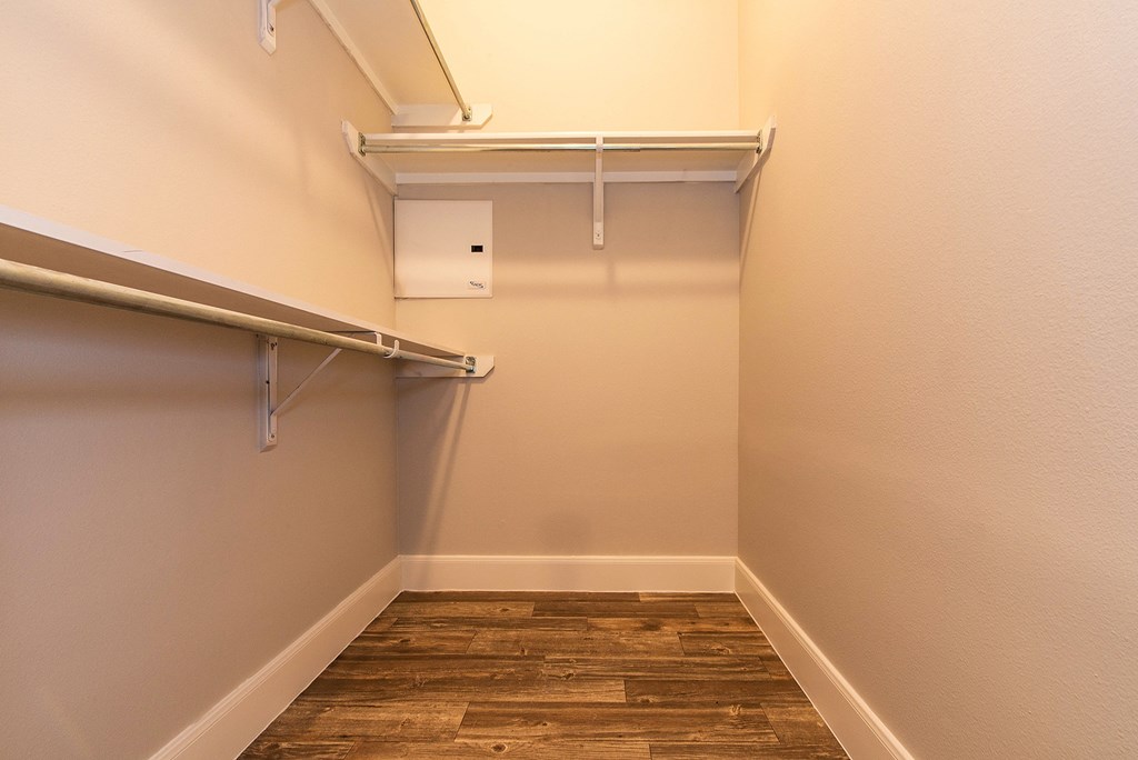 a spacious walk in closet in a home with wood flooring and a white wall