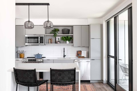 A modern kitchen with a white countertop and black chairs.