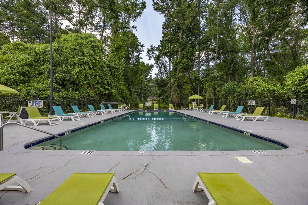 A large outdoor swimming pool surrounded by trees and lounge chairs. at Peachtree Place Apartments, Columbia