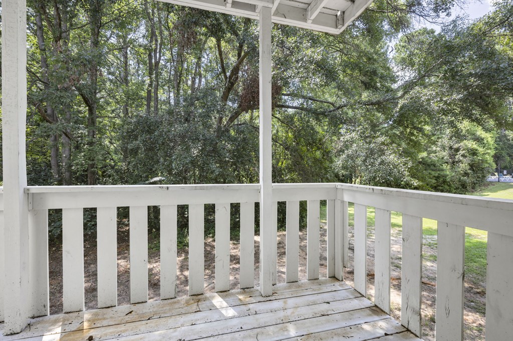 A white wooden porch with a roof and railings overlooking a wooded area. at Peachtree Place Apartments, Columbia, South Carolina