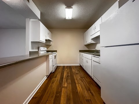 A kitchen with white appliances and wooden floors.