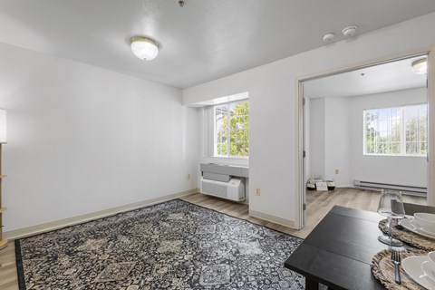 the living room and dining room of a house with white walls and a black rug