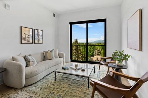 A living room with a couch, a coffee table, and a view of the outdoors through a large window.
