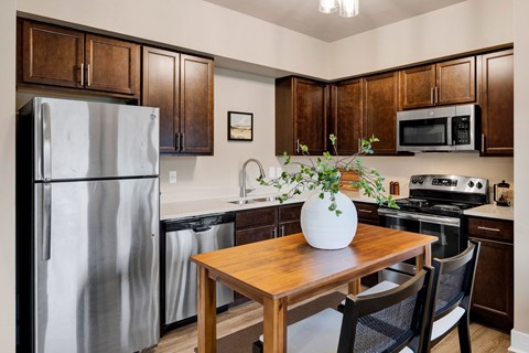 A kitchen with a wooden table and chairs, a refrigerator, a microwave, and a stove.