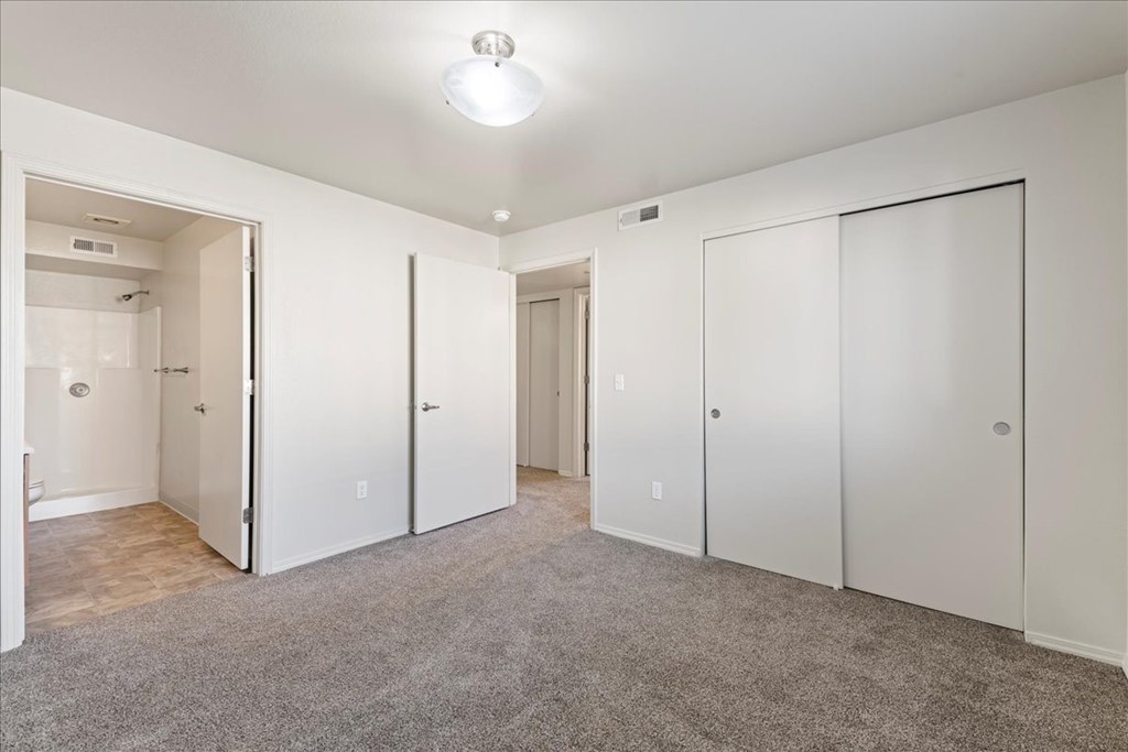 A white bedroom with a grey carpet and four doors.