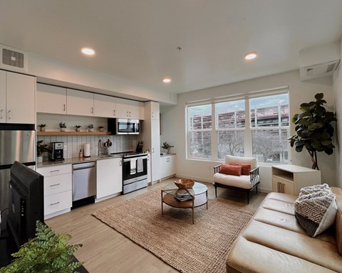 An open-style living room with view into the  kitchen, cozy seating area with a coffee table, and large windows at The Lucy, Idaho, 83702