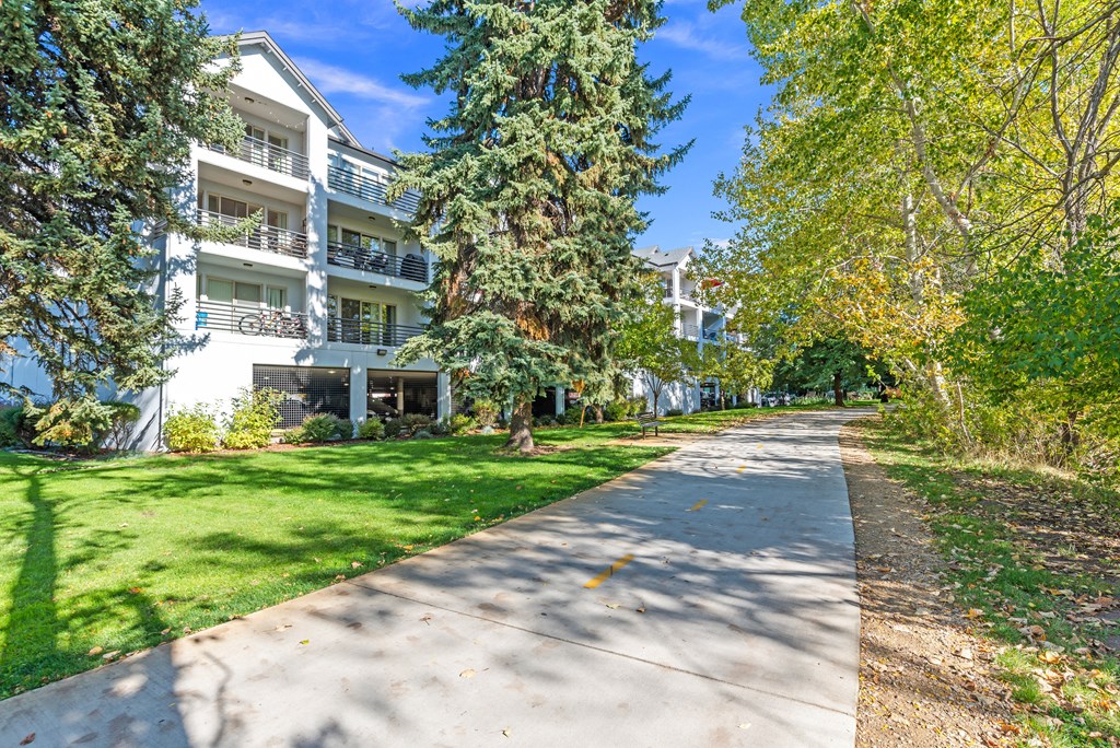 a sidewalk in front of an apartment building with trees and grass