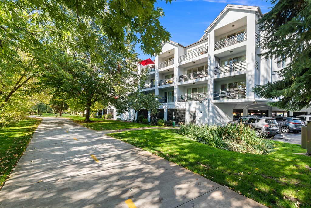 a sidewalk in front of a white apartment building with trees and grass