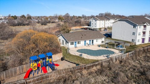 A playground with a red slide is in front of a building with a pool.