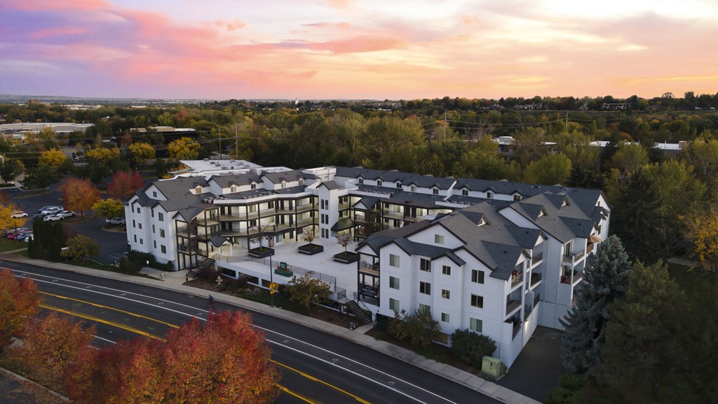 an aerial view of a white and gray apartment building with a sunset in the background