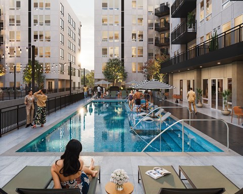 A woman in a floral dress sits by a pool in a courtyard surrounded by buildings.