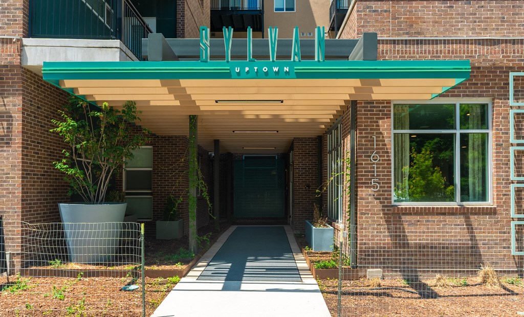 the red brick entrance to the property with a green awning at Sylvan Uptown, Denver, CO