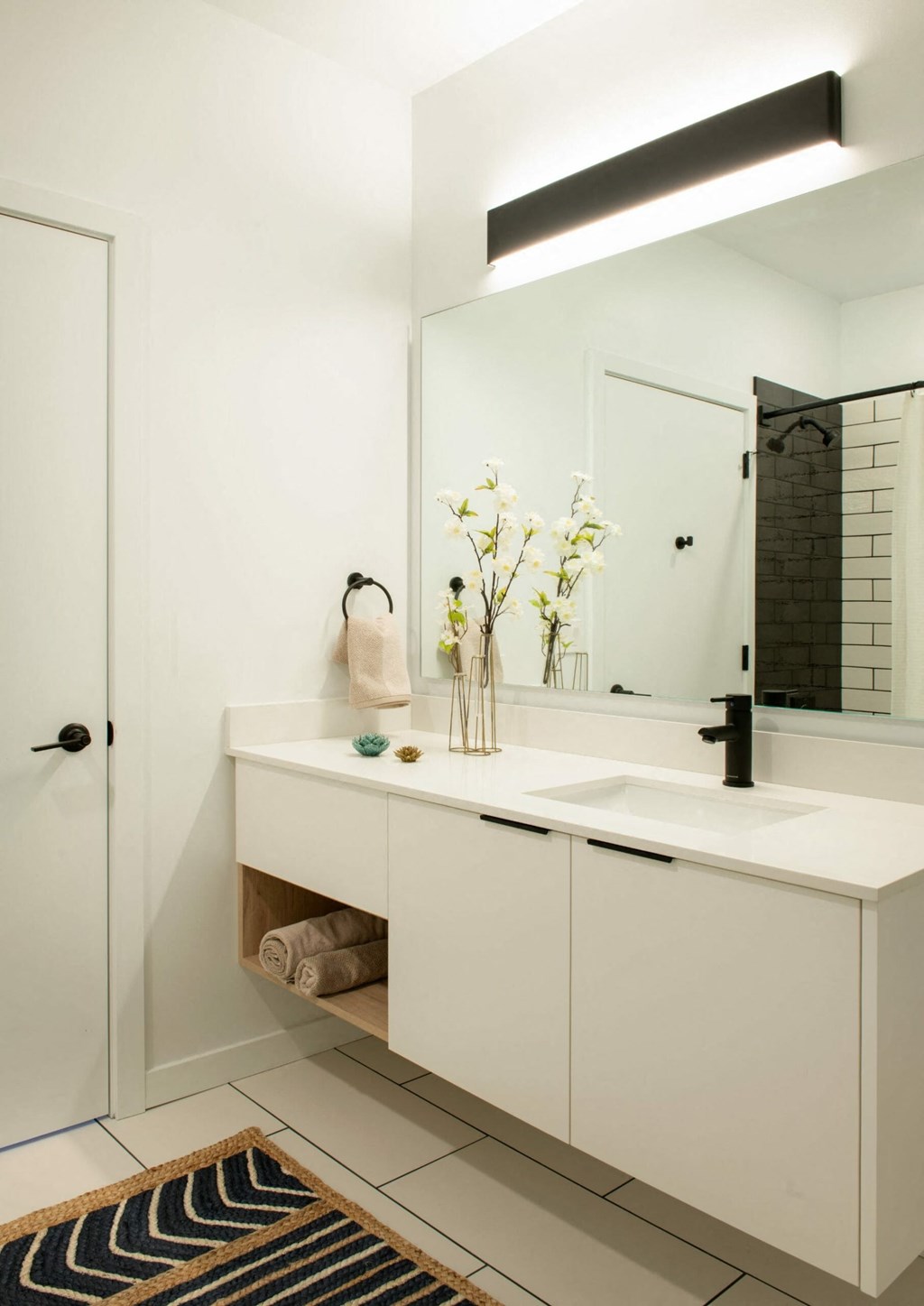 a small bathroom with white cabinets and a black and white rug