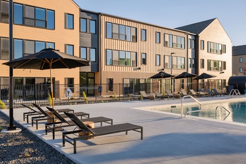 A pool area with sun loungers and umbrellas in front of a building.
