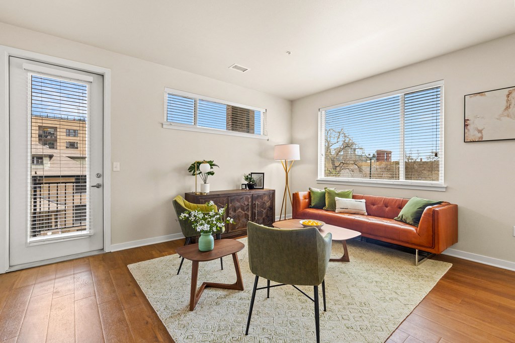 Spacious living room with a couch and chairs surrounding in natural light from the windows and door leading out to the balcony at Sylvan Uptown, Colorado