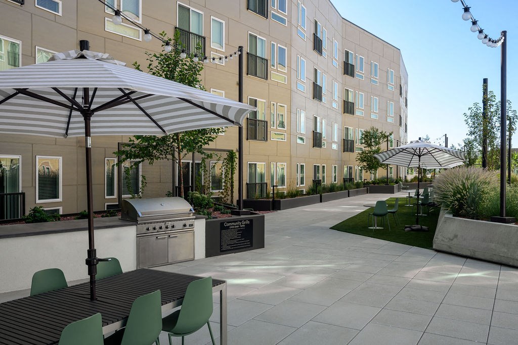 a patio with tables and umbrellas in front of an apartment building at Crosshatch, Garden City, ID, 83714