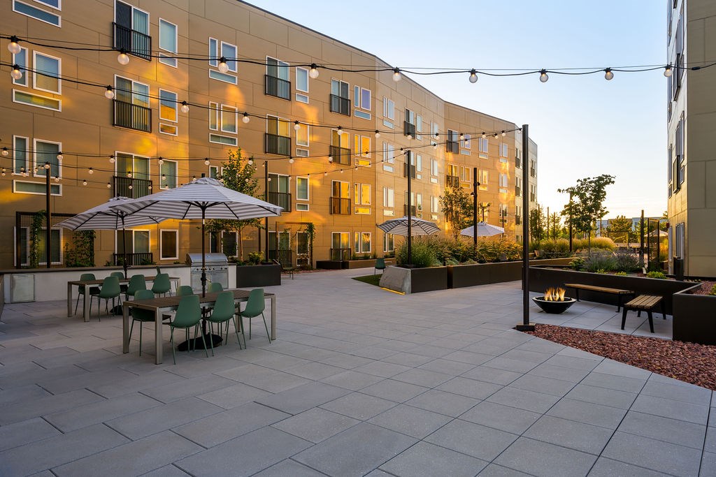 a courtyard with tables and umbrellas in front of an apartment building