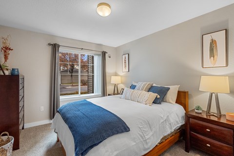 A bedroom with a bed, nightstands, and a window with a view of a tree.