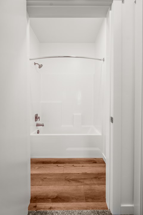 A white bathroom with a wooden floor and a white bathtub at Silverbrook Apartments, MT 59901