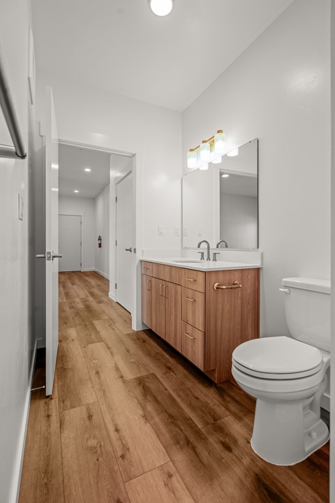 A spacious bathroom with wooden floors, a wooden vanity, and a mirror above it at Silverbrook Apartments, Kalispell