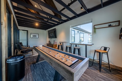 A shiny wooden air hockey table is in the middle of a room with a black trash can and a window. at Silverbrook Apartments, Montana, 59901