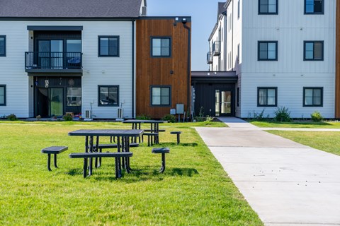 A series of picnic tables are set up on a green lawn in front of a white building. at Silverbrook Apartments, Montana, 59901