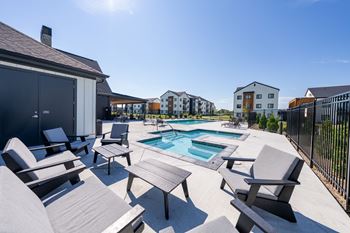 A sunny day at a poolside with chairs and a table. at Silverbrook Apartments, Kalispell, MT