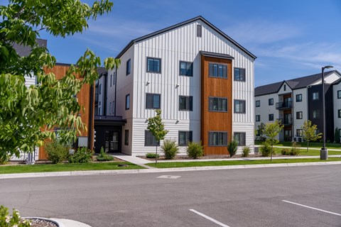 A modern building with a white facade and a brown door is surrounded by other buildings and trees. at Silverbrook Apartments, Kalispell, MT, 59901