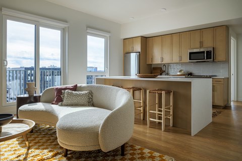 a living room with a couch and a kitchen with a bar and a large window