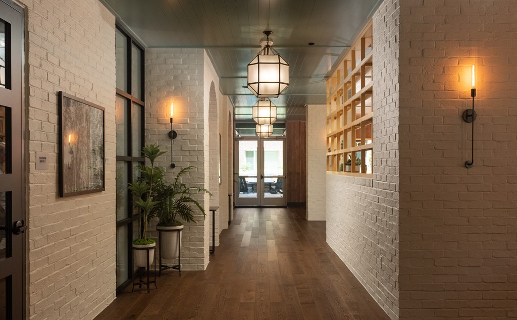 Long white brick hallway with wood flooring and geometric pendant lighting leading to resident lounge at Sylvan Uptown, Colorado
