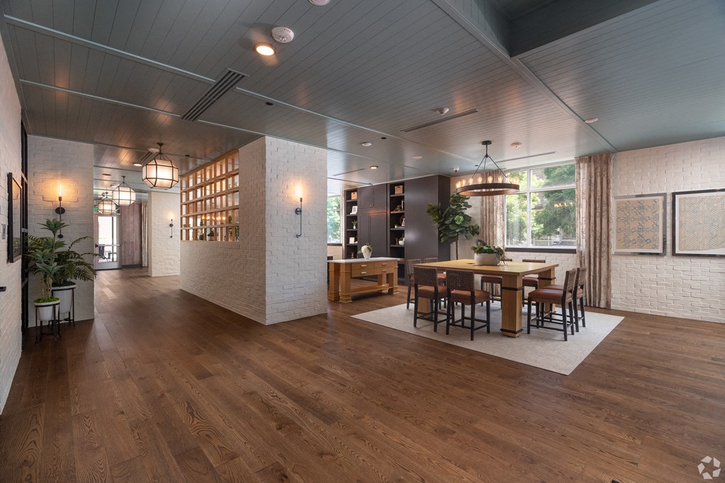 View of the resident lounge with white brick walls, square wooden table with cognac colored chairs and wooden floors  at Sylvan Uptown, Denver