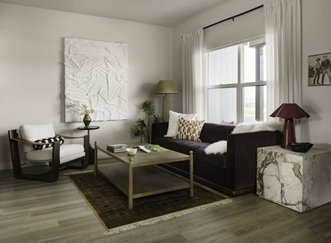 A living room with a white chair, a black couch, a coffee table, and a large painting on the wall.